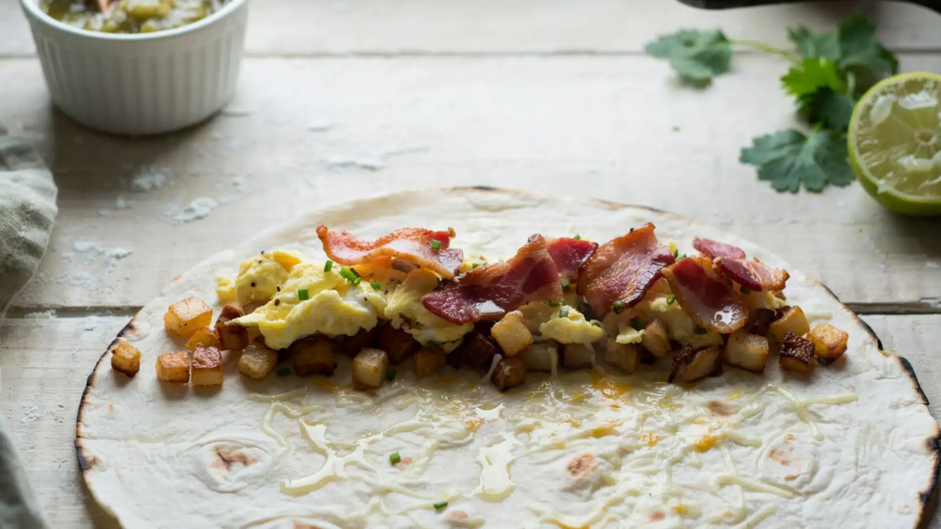 A breakfast burrito filled with bacon, scrambled eggs, and diced potatoes, wrapped in a soft tortilla.