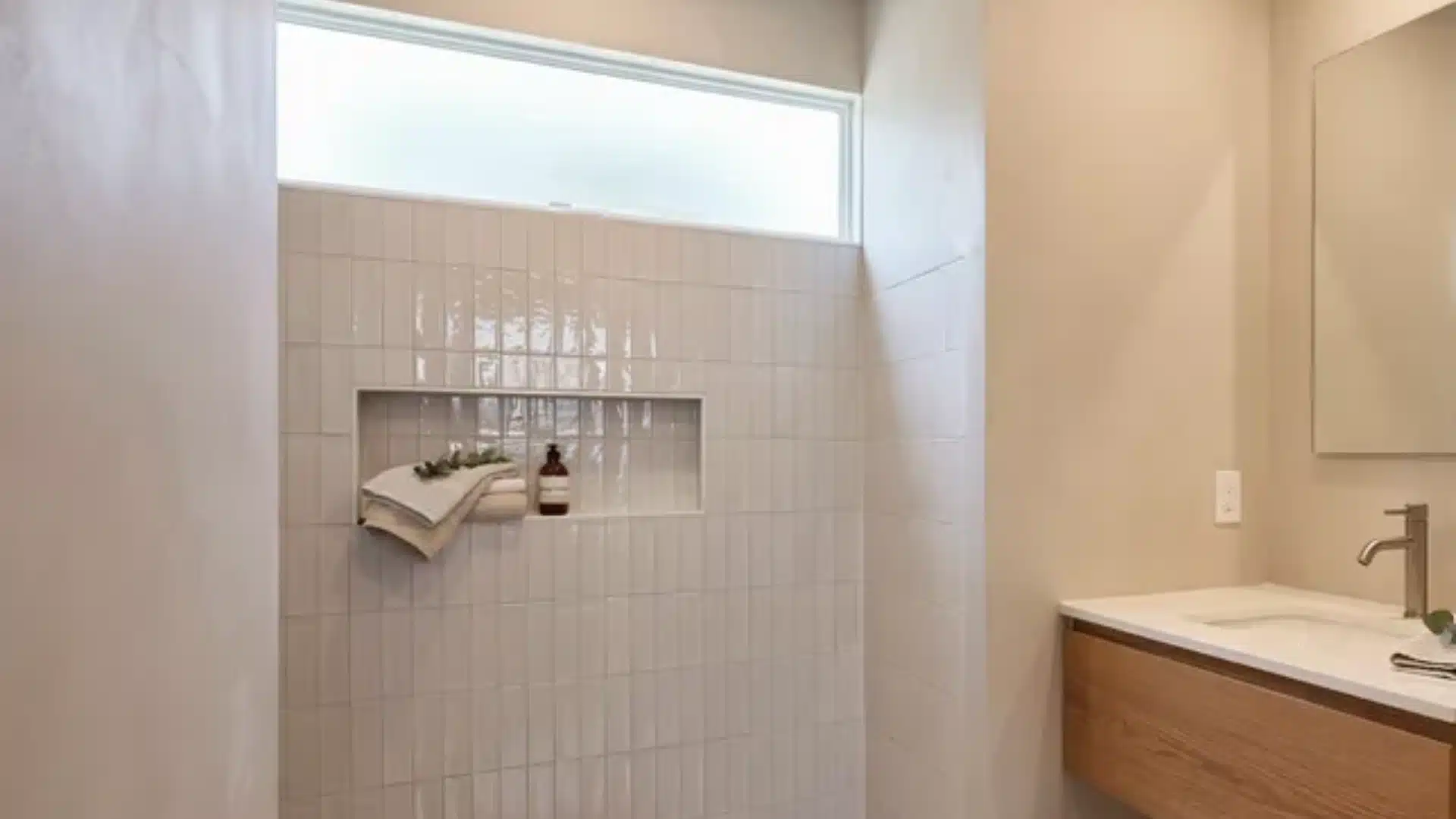 Minimal modern bathroom with light tiled walls, recessed shower niche, small window, wood vanity and neutral tones