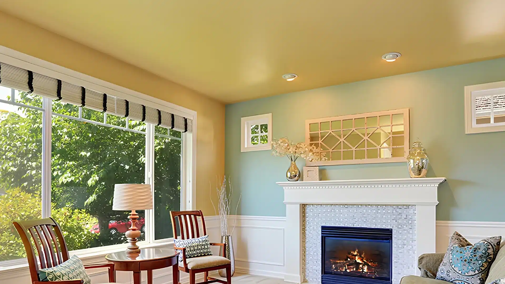Living room with a yellow ceiling, a fireplace, large window overlooking greenery, and two wooden chairs