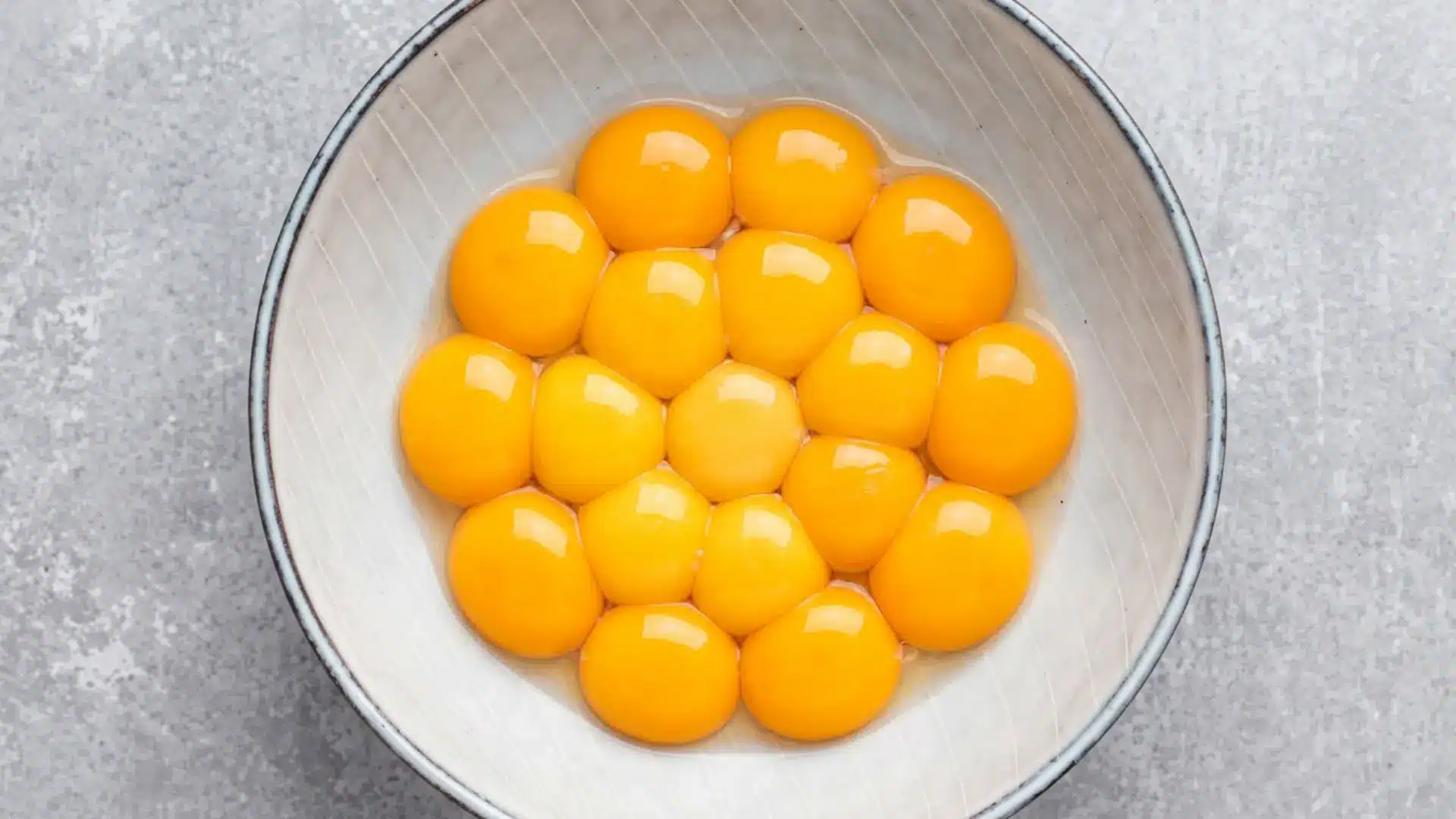Multiple fresh egg yolks separated into a white ceramic bowl on a gray surface