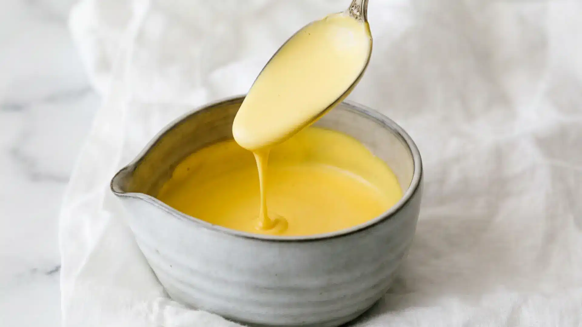 smooth hollandaise sauce ready to be drizzled over eggs benedict
