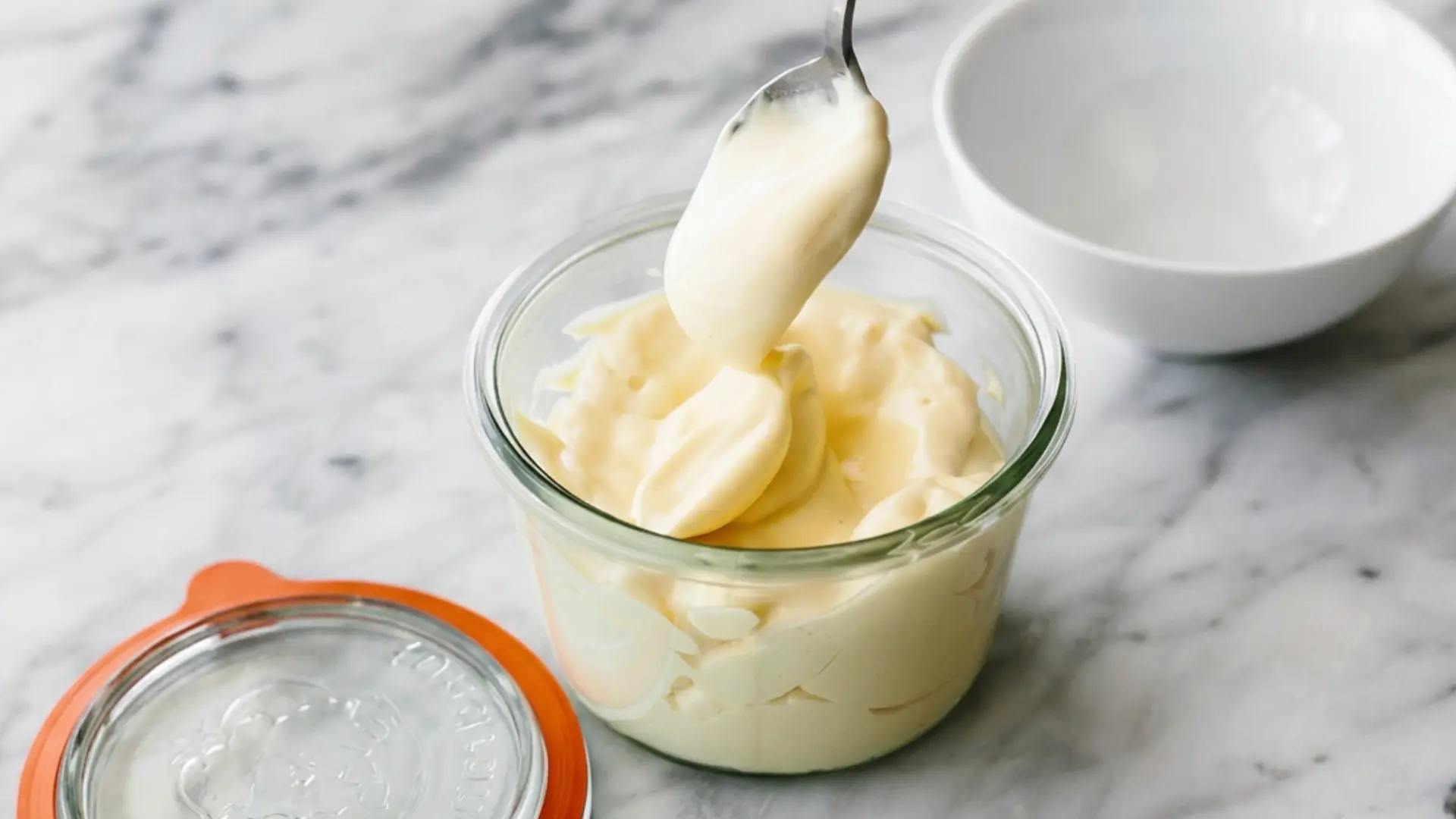 omemade mayonnaise in a glass jar with a spoon and fresh lemon beside it