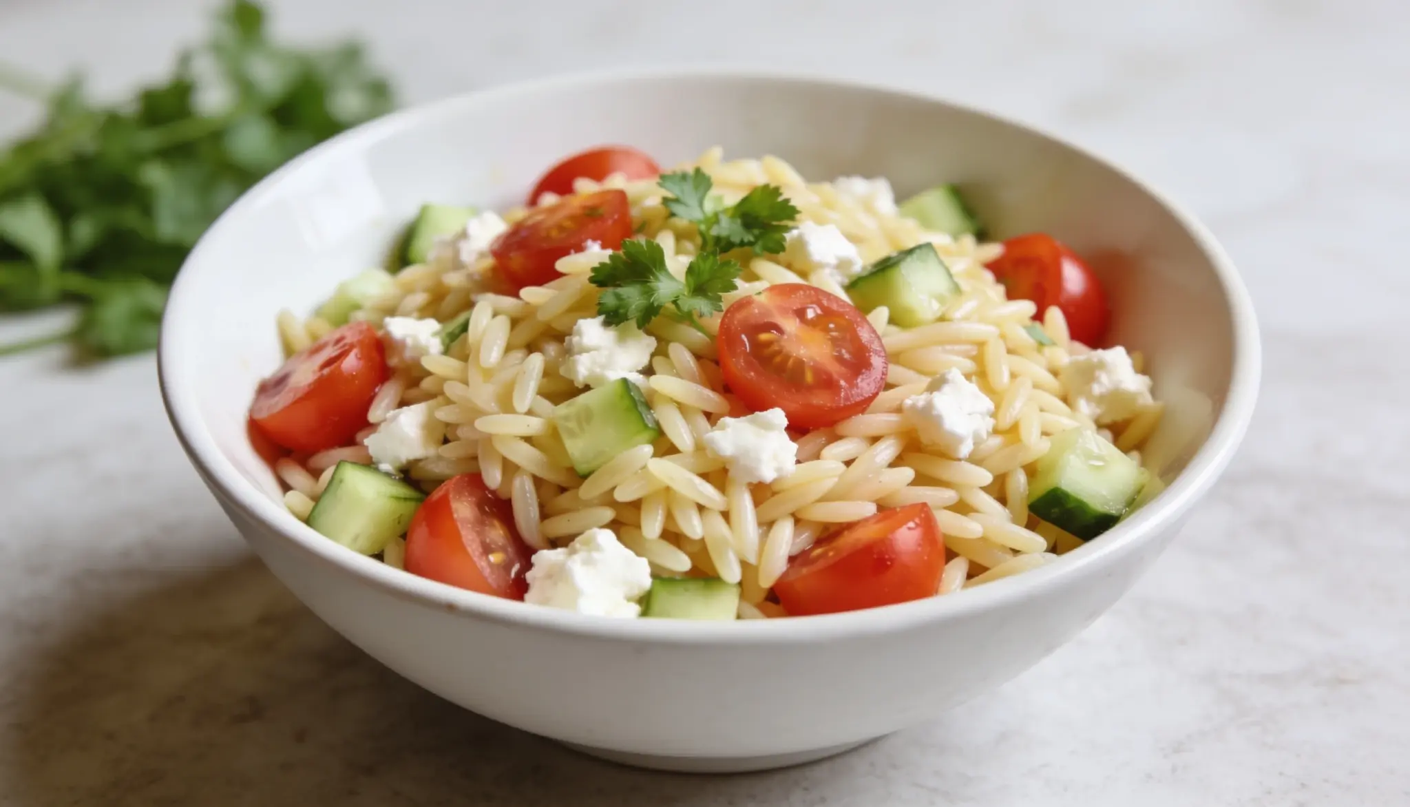 A fresh orzo salad with cherry tomatoes, cucumber, feta cheese, and parsley, served in a white bowl. A light, Mediterranean-inspired dish that's perfect for lunches, picnics, or side servings.