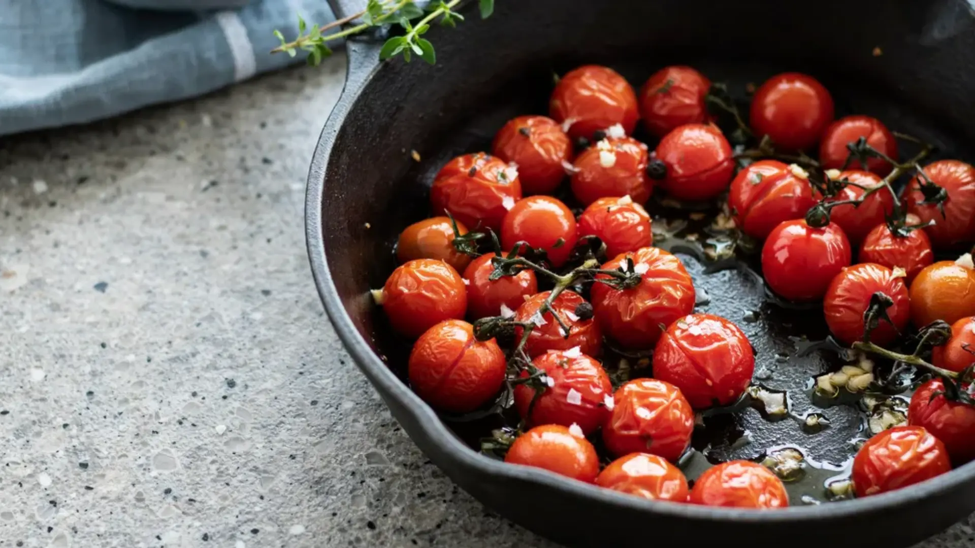 Cherry tomatoes are roasted in a cast-iron skillet with herbs and garlic.