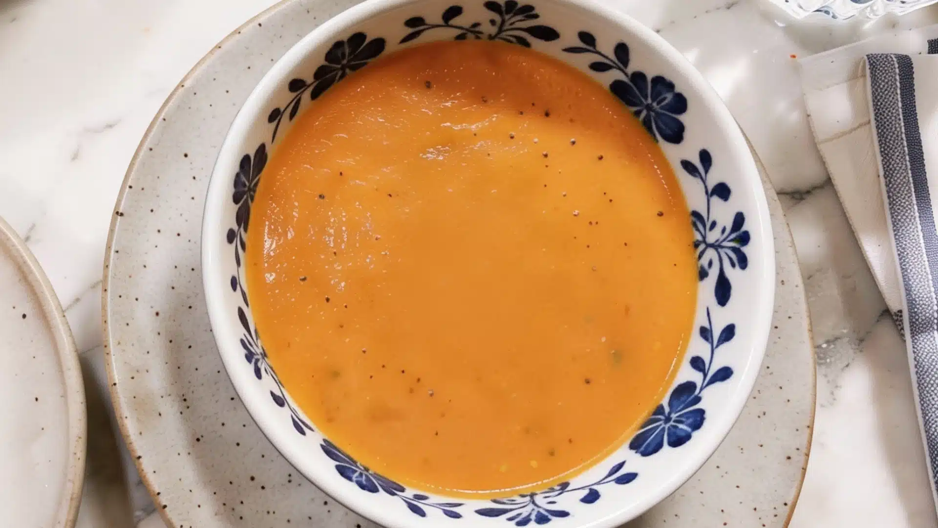 A red lentil tomato soup bowl filled with hot soup accompanied by a slice of lemon for added flavor.