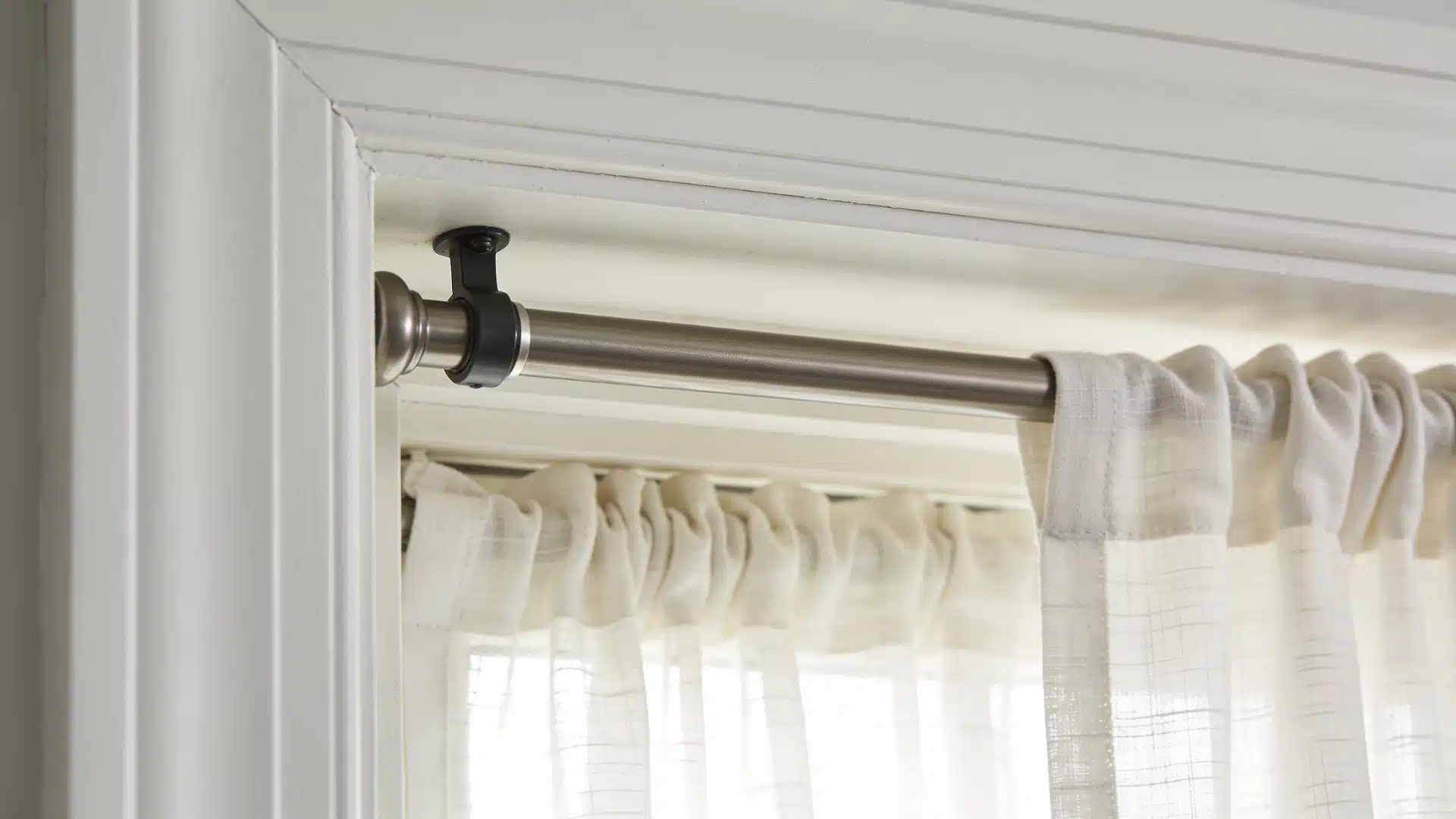 Tension rod installed inside a window recess holding sheer curtains without screws or wall brackets