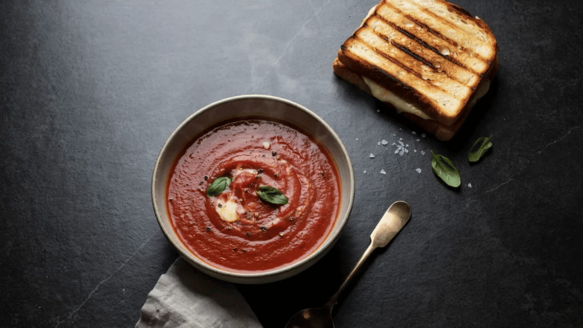 tomato soup served with grilled cheese, basil garnish, and cream swirl in a bowl on a dark tabletop
