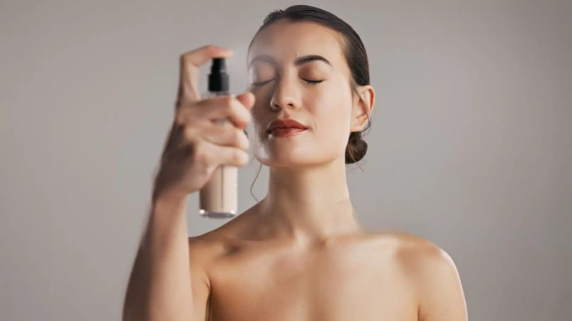 Close-up beauty portrait of model applying finishing spray for glowing skin in soft studio lighting