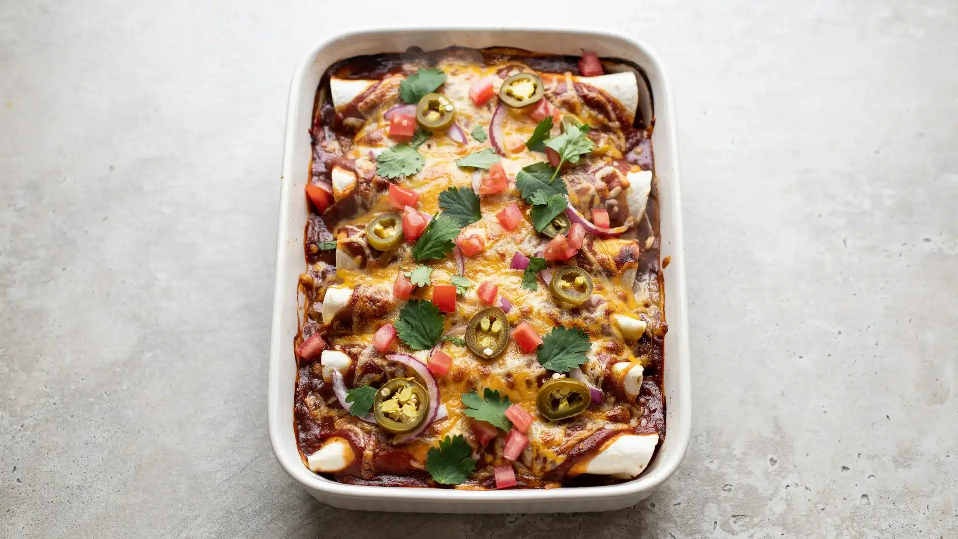 A close-up of a casserole dish containing Mexican enchiladas, layered with sauce and melted cheese, ready to serve.