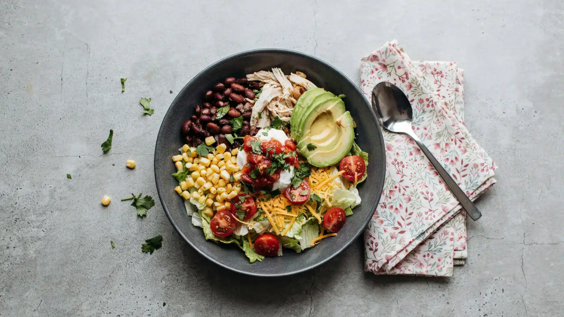 A colorful bowl of Mexican chicken salad with diced avocado, sweet corn, and ripe tomatoes, garnished with cilantro.