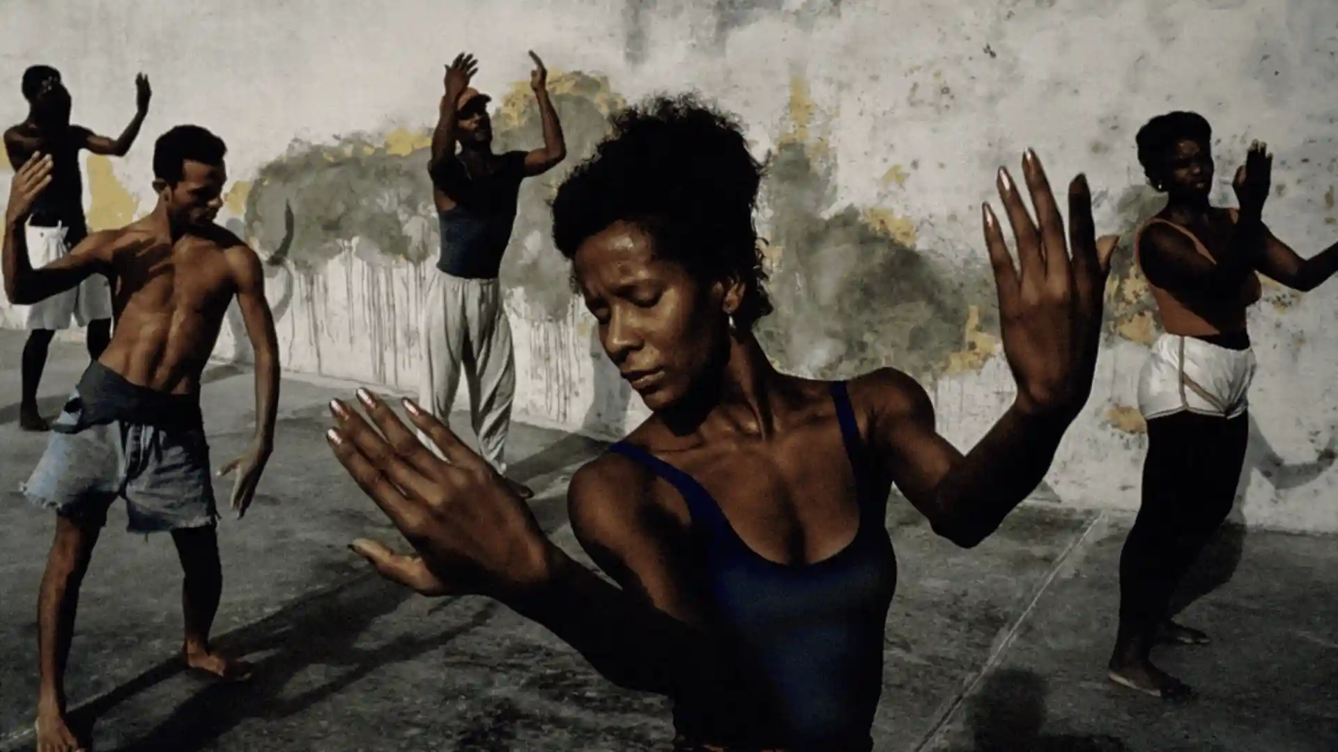 A group of people are dancing in front of a distressed concrete wall.