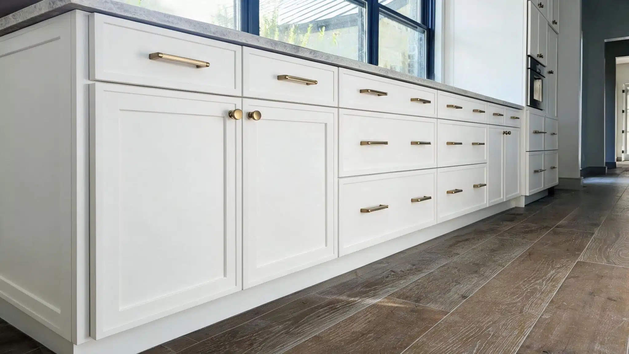 A modern kitchen featuring slim-frame shaker doors, white cabinets, and warm wooden flooring.