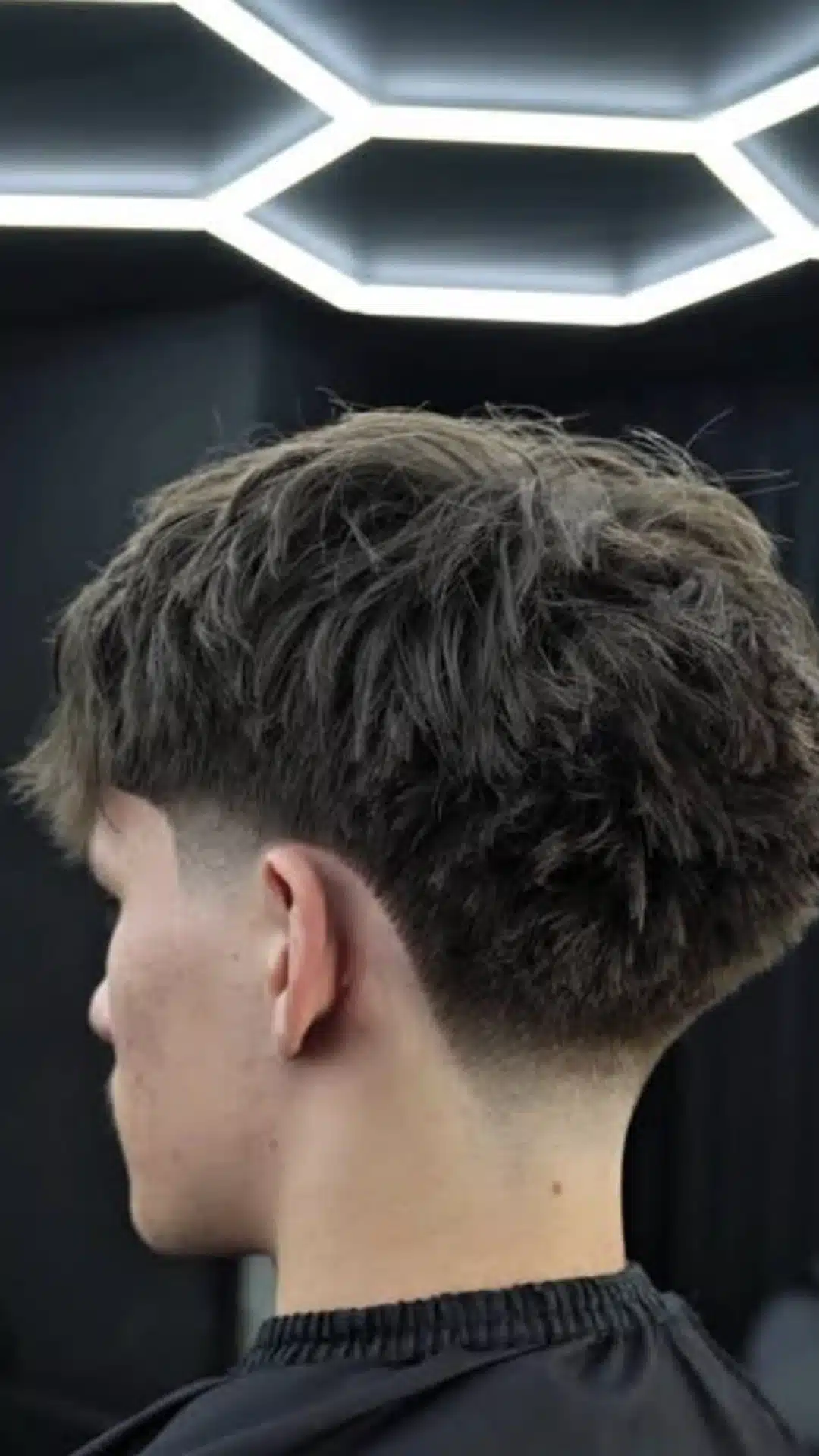 Back and side view of a man with a low taper fade haircut featuring textured hair on top