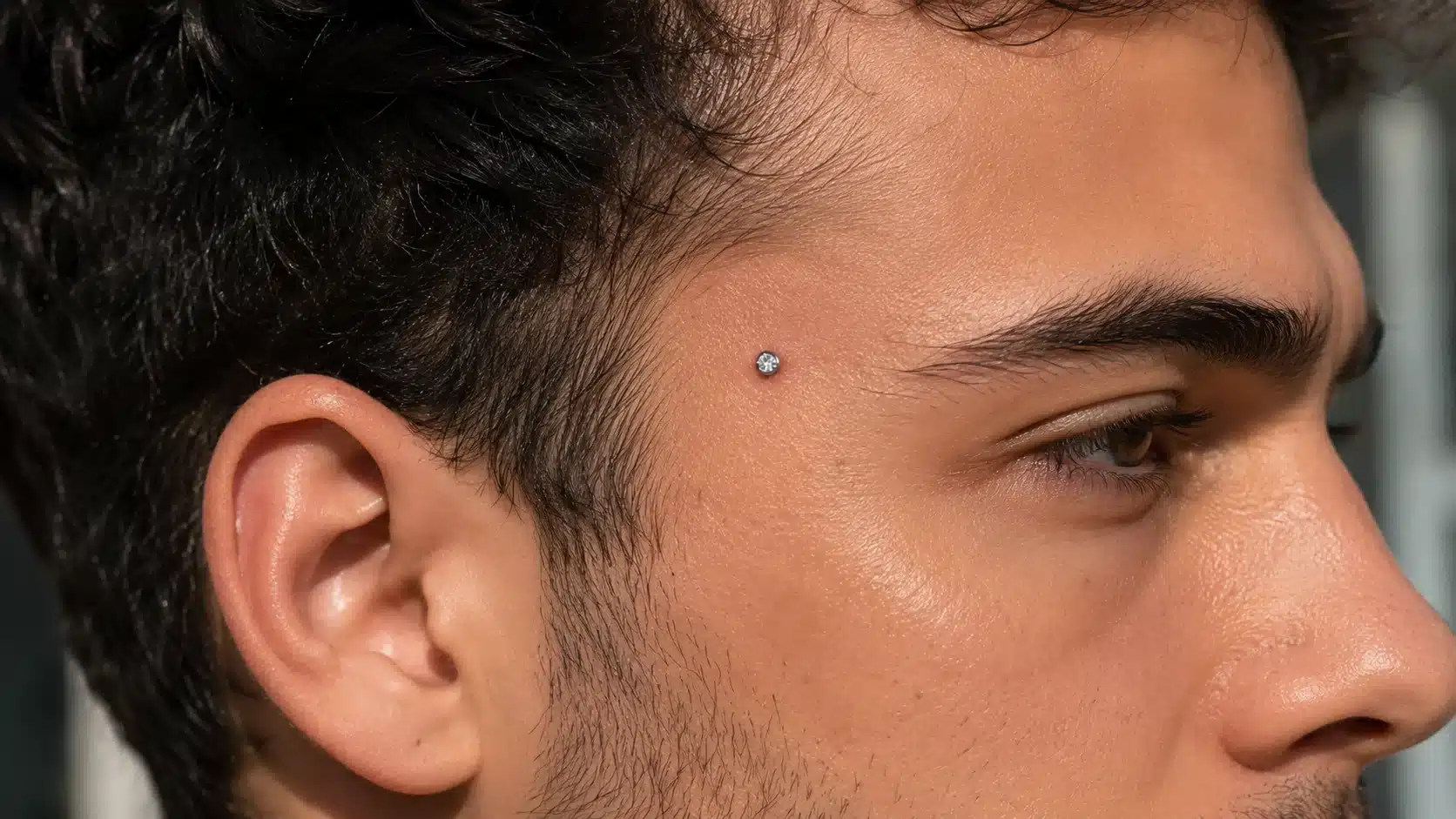 Close-up of a man showcasing a temple piercing, highlighting the jewelry's design and placement.
