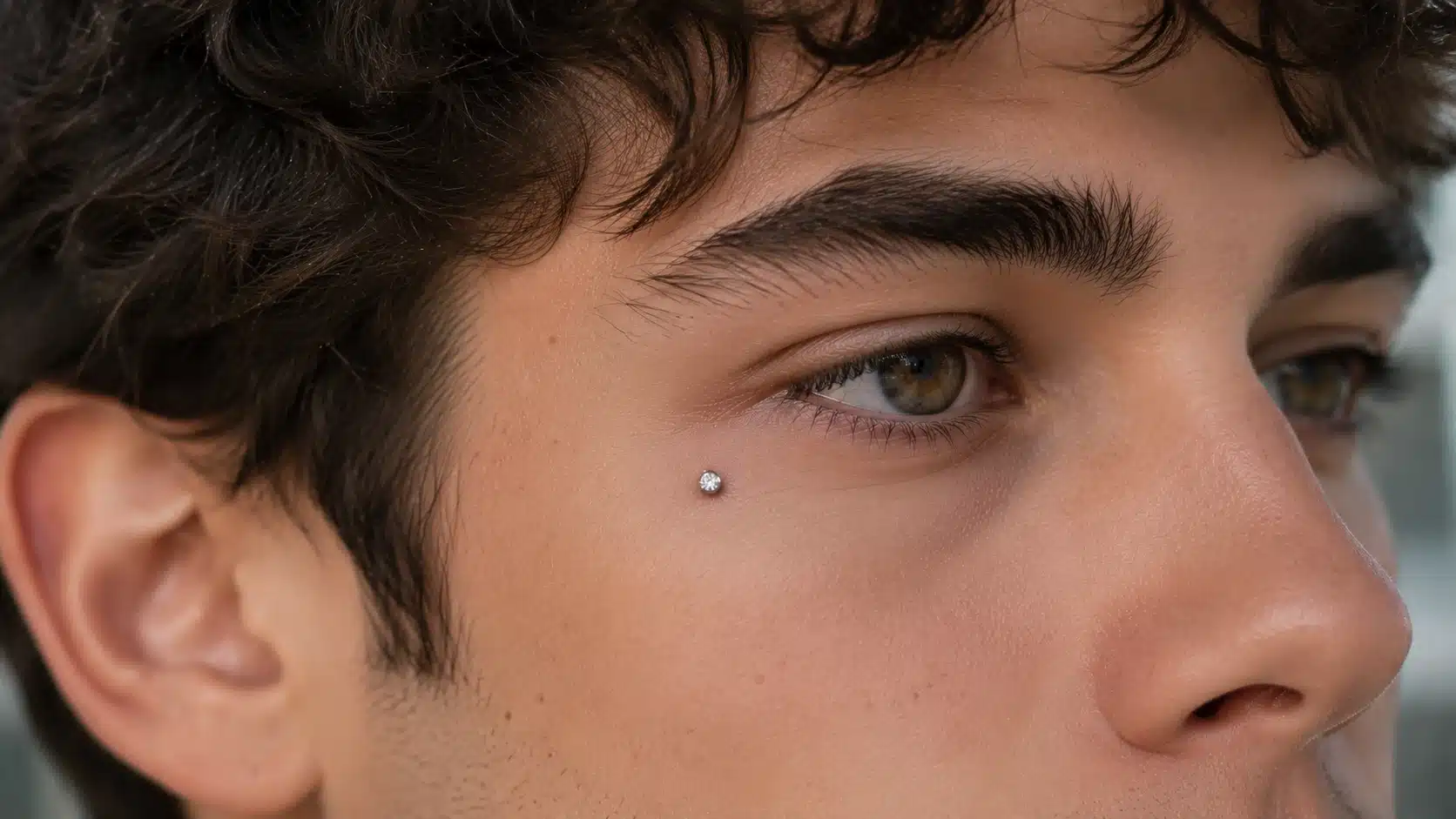 Close-up of a young man showcasing an under-eye piercing on his face, highlighting the unique facial adornment.