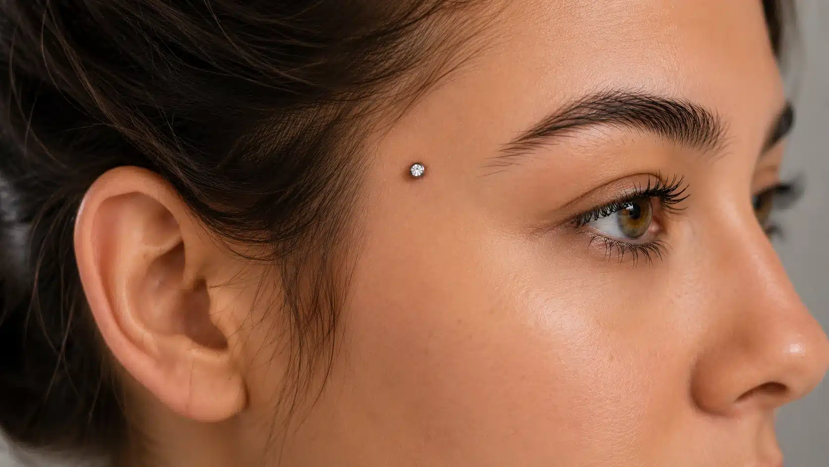 A woman displaying a dermal piercing on temples, highlighting the unique jewelry.