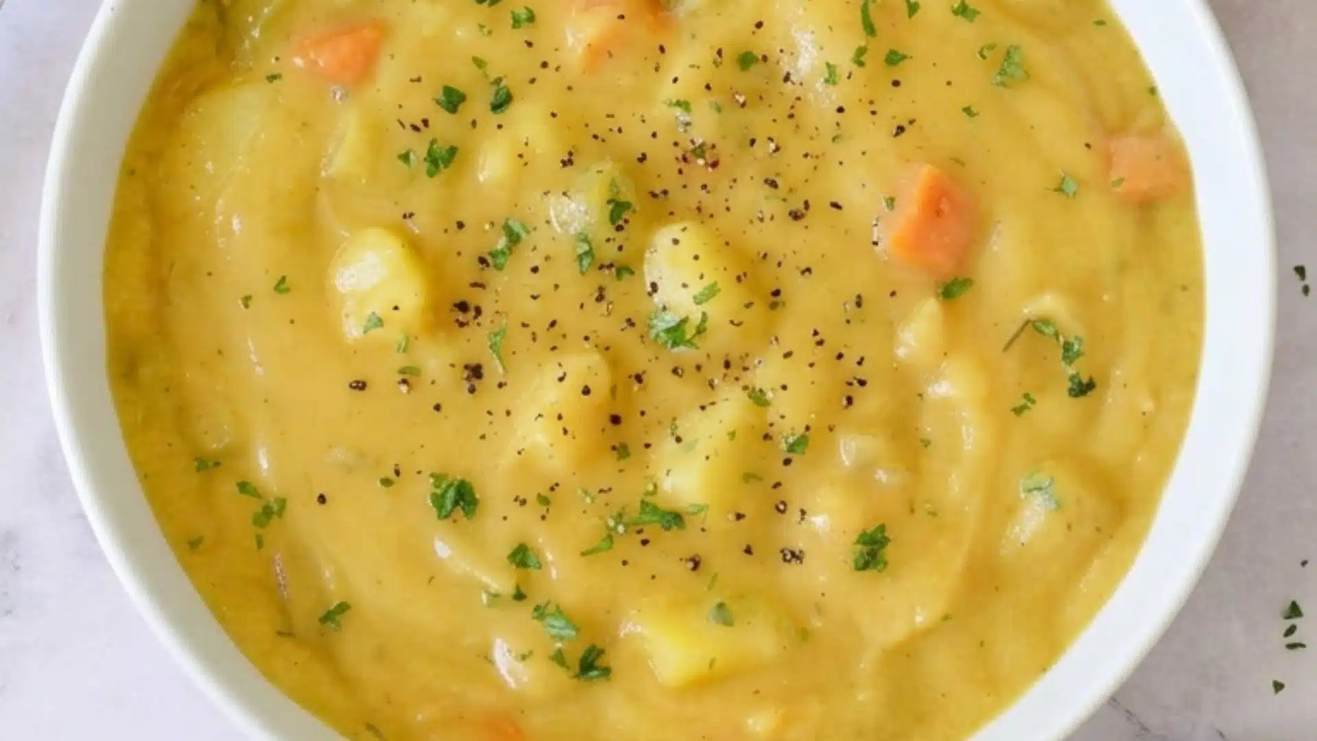 Creamy vegetarian potato soup with carrots, potatoes, herbs, and black pepper, served with sliced bread and butter.