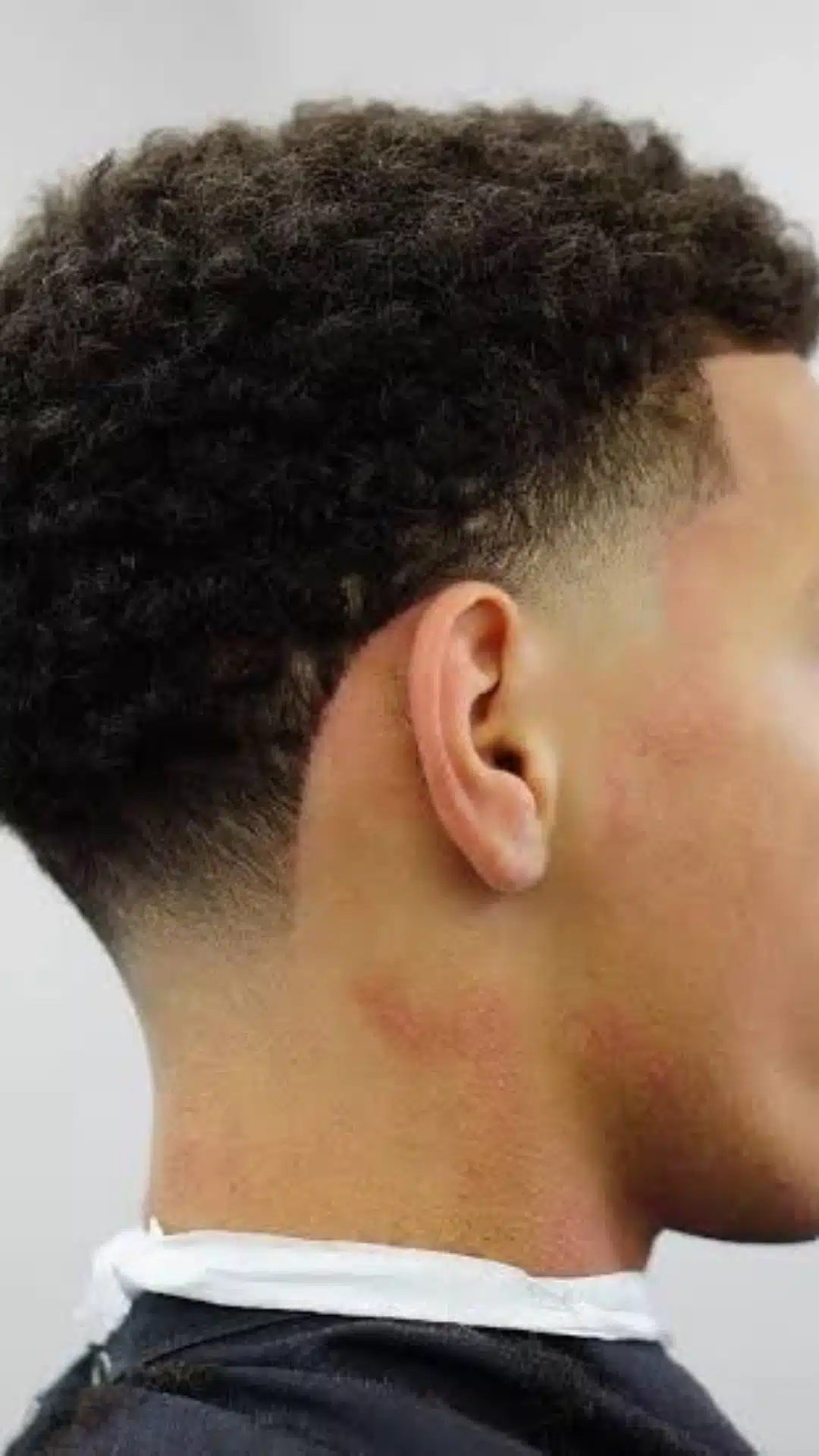 Side and back view of a man with a high taper fade haircut featuring short curly hair