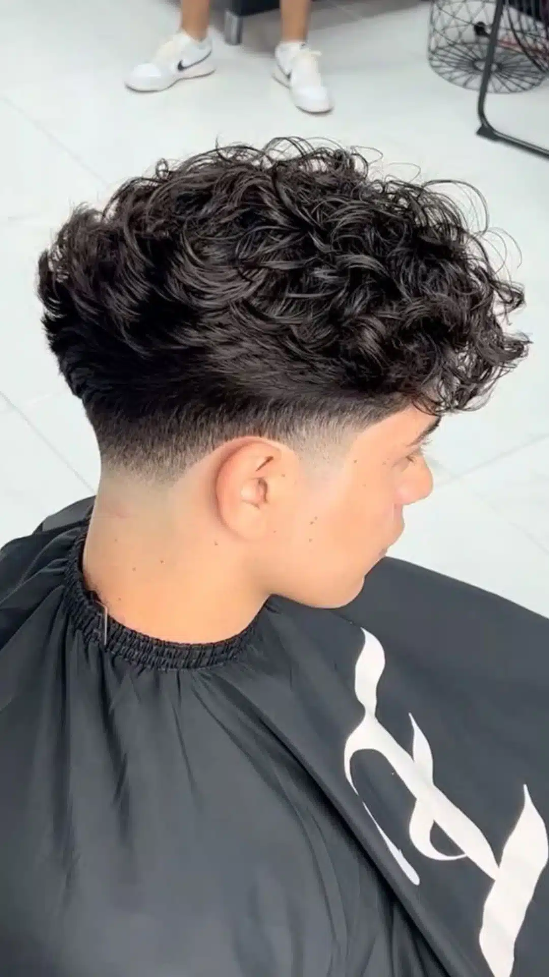 Side and back view of a man with a mid taper fade haircut featuring curly textured hair