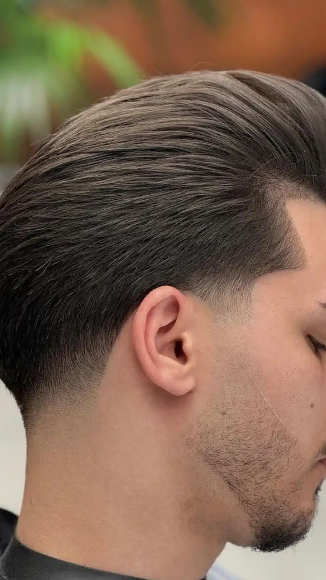 Side profile of a man with a slick back taper haircut featuring neatly combed hair on top and a clean gradual taper around the sides and neckline